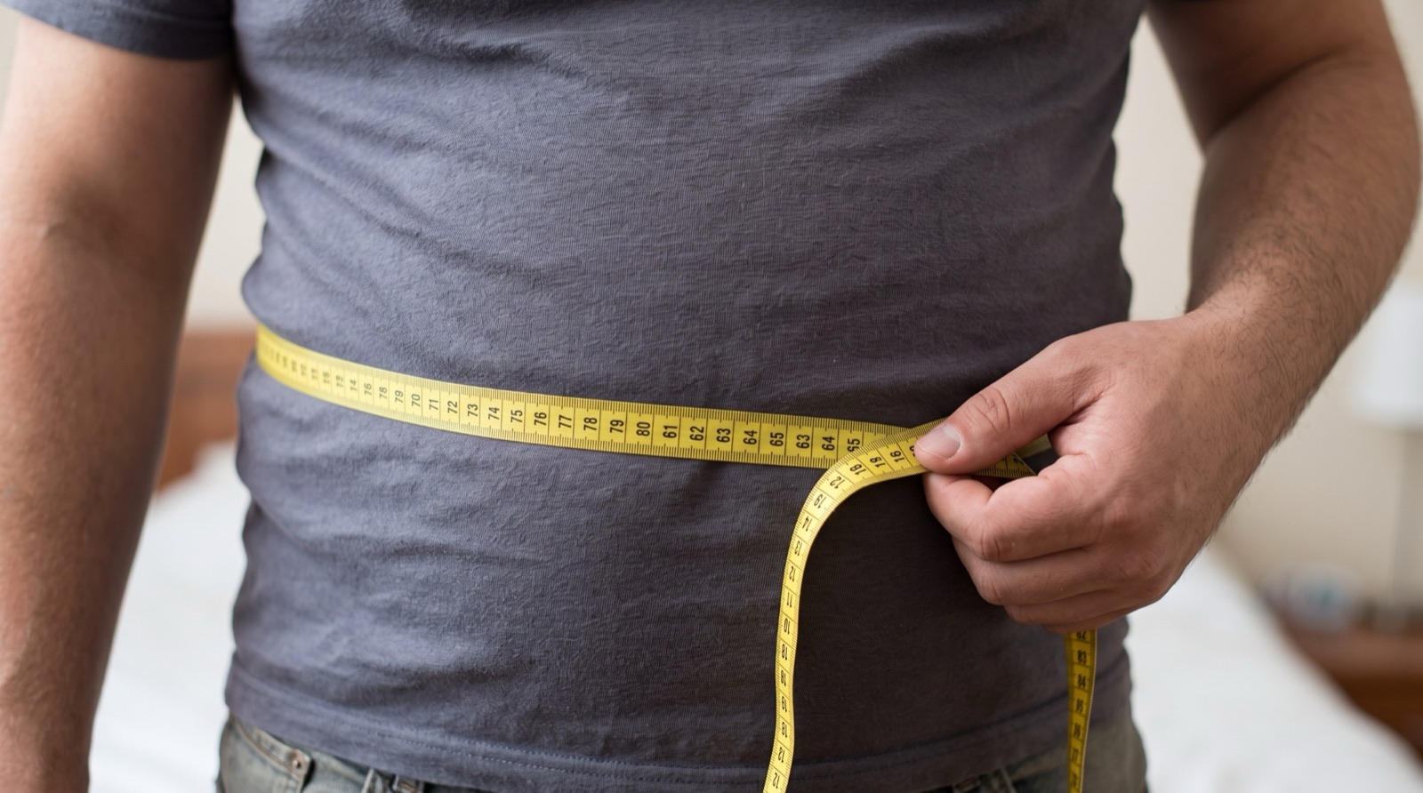 Man measuring his waist with a tape measure at navel level to track visceral fat